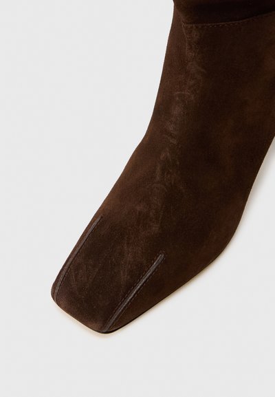 Stivaletto in camoscio marrone con punta quadrata, dotato di due piccole linee di cucitura decorative sulla parte superiore e una texture liscia.