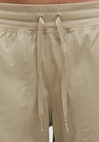 Beżowe szorty o prążkowanej fakturze, z elastycznym pasem zakończonym metalowymi agletami i przeszytymi bocznymi szwami.