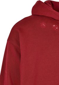 Felpa rossa con cappuccio, caratterizzata da una texture morbida e piccoli segni di usura sul tessuto. Progettata con cappuccio regolabile e una vestibilità comoda.