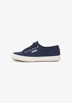 Zapatilla de lona navy con suela de goma blanca, puntera redonda, diseño de cordones y pequeño parche de logo en el costado. Detalles de tela texturizada.