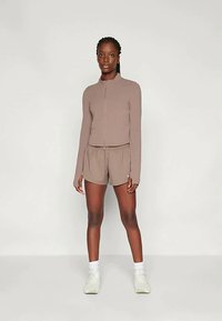 Kerge pruuni värvi lukuga jakk pikkade varrukatega, millele on juurde sobitatud lühikesed püksid. Pehme kangas, minimaalne disain ja valged spordijalatsid.