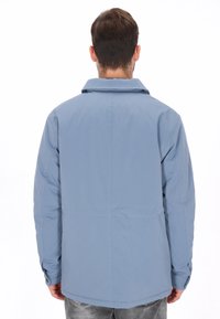 Chaqueta azul claro de manga larga con cuello puntiagudo, corte recto y puños con botones. Textura suave y diseño minimalista.