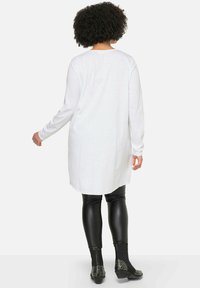 Wit tuniek met lange mouwen en een ronde zoom, gecombineerd met glanzende zwarte leggings en gestifte enkellaarsjes. Gladde textuur met een relaxed fit.