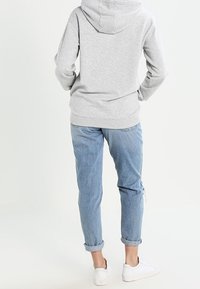 Sudadera con capucha gris, de corte holgado; combinada con jeans de tiro bajo en azul claro con los puños enrollados y zapatillas blancas. Enfocado en la comodidad casual y la simplicidad.