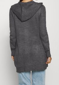 Grå stickad cardigan med huva, med en strukturerad yta och ribbade ärmslut och nederkant. Långa ärmar, medellång design.