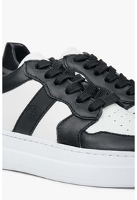 Czarno-białe skórzane sneakersy o niskiej cholewce, z fakturowaną powierzchnią i czarnymi sznurowadłami. Posiadają trwałą gumową podeszwę oraz wyraźne perforacje.