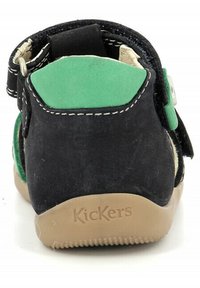 Zapato infantil de ante negro con detalles en verde, correa ajustable y suela de goma beige. Logotipo de la marca "Kickers" grabado en el talón.