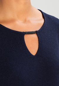 Pull bleu marine avec un col rond et une découpe en forme de trou de serrure, accentué par une sangle texturée noire. Tissu doux en maille avec une texture uniforme.