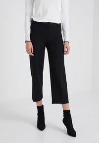 Pantalon noir court au style épuré, confectionné en tissu extensible, associé à des bottines noires côtelées à la cheville. Design simple, allure soignée.