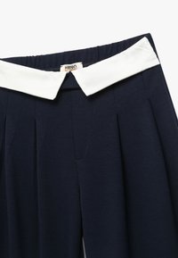 Pantalones navy con una cinturilla blanca con cuello, diseño plisado y tejido texturizado. Incluye detalles de costura y una etiqueta en el interior.