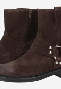 Bottines en suede marron foncé avec une fermeture éclair, des détails en sangle, des éléments en métal, et des accents cousus le long de la semelle pour une texture supplémentaire.