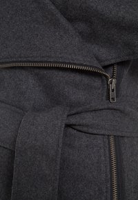 Dunkelgrauer Wollmantel mit Wickeldesign, der mit einem auffälligen Reißverschluss und einem Stoffband ausgestattet ist, das die weiche Textur und klaren Linien hervorhebt.