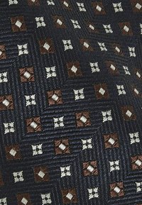 Culoare geometrică a unui material cu elemente maronii, albe și bleumarin.Țesătură texturată cu pătrate și cruci prin întreaga compoziție.