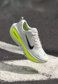 Chaussure Nike ZoomX blanche avec des accents noirs et une semelle jaune fluo. Elle présente une tige texturée, une semelle rembourrée et des lacets légers.