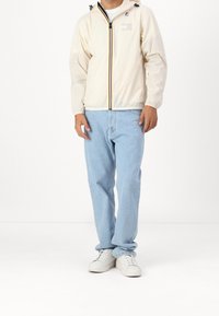 Bílá lehká bunda s barezným zipem a logem, doplněná světle modrými džínami a bílými teniskami, s volným střihem.