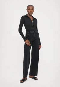 Black long-sleeve polo with button placket paired with high-waisted, wide-leg black jeans and black sandals, smooth fabric, fitted design.
