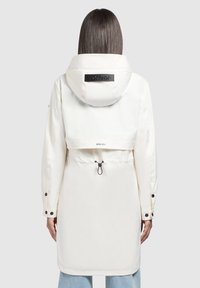 Giacca impermeabile bianca con cappuccio, caratterizzata da una patch con logo nera, vita regolabile con coulisse e polsini con bottoni a pressione. Design lungo e aerodinamico.