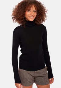 Schwarzer Rollkragenpullover aus weichem Stoff, mit langen Ärmeln und figurbetonter Passform, kombiniert mit braunen, strukturierten Shorts.