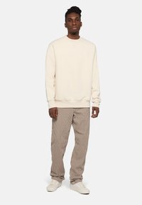 Sudadera color crema con cuello redondo, combinada con pantalones beige a rayas y zapatillas blancas. Presenta un ajuste relajado y puños acanalados.