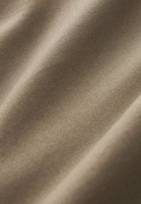 Beige kangas, jossa on sileä, tekstuurinen pinta, näyttäen kudontakuvioita ja hillittyjä valonheijastuksia. Pehmeä ja joustava materiaali.