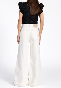 Haut en dentelle florale noire avec manches à volants, associé à un pantalon blanc à jambes larges avec ourlets retroussés et poches arrière.