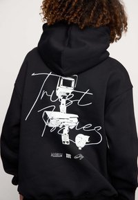 Felpa nera con cappuccio caratterizzata da un design grafico con testo bianco "Problemi di fiducia" e rappresentazioni artistiche di una macchina fotografica e altre attrezzature.