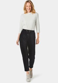 Zwarte jogpants met een taillekoord, gemaakt van zachte stof. Gecombineerd met een witte, lange mouwen top en lichtgrijze sneakers.