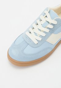 Svijetloplavi sneakersi od suedea i kože s bijelim detaljima, ravne vezice i kontrastna smeđa guma. Zaobljeni vrh i podstava od pjene.