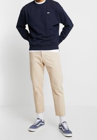 Sudadera azul marino con cuello redondo y logo bordado, combinada con pantalones beige claro de corte ajustado y zapatillas azul marino con detalles en blanco.