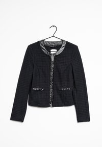 Veste noire texturée avec un col rond, bordure noire brillante, fermeture éclair et deux poches avant. Suspendue à un crochet sur un fond blanc.