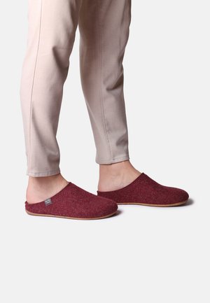 Chaussons en feutre rouge à enfiler avec une texture douce et une semelle en caoutchouc flexible, associés à un pantalon tailleur de couleur claire.