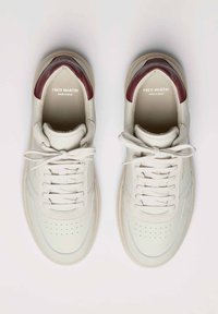 Sneakers bianchi in pelle con inserto rosso scuro sul tallone, design con lacci, punta perforata e logo sulla linguetta. Suola piatta color crema.