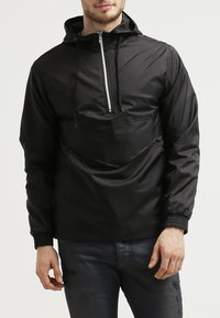 Zwart pullover jack met capuchon, halve rits aan de voorkant, elastische manchetten en een voorzak. Glad, lichtgewicht materiaal met een matte afwerking.