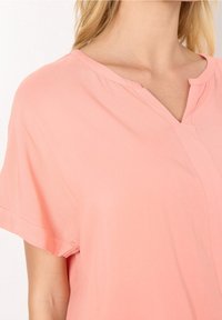 Blusa color pesca con scollatura a V, maniche corte e vestibilità rilassata. Realizzata in tessuto leggero, presenta dettagli di cucitura sottili.