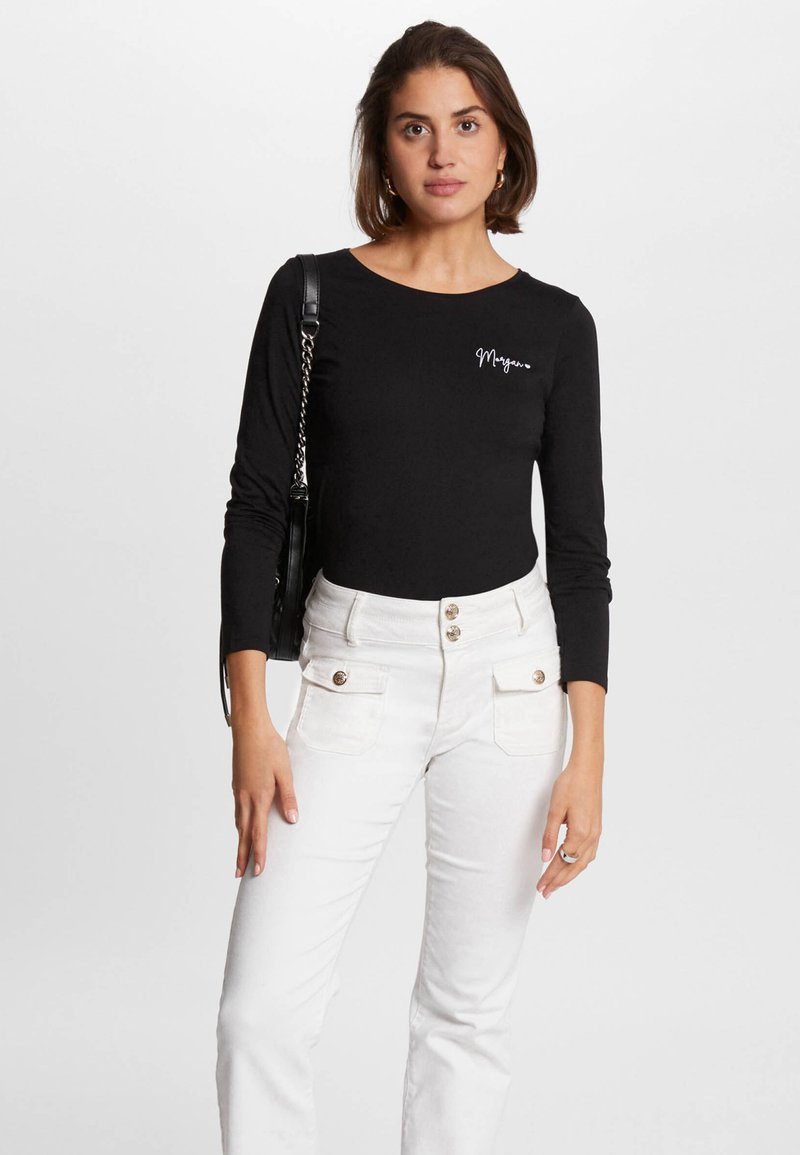 Maglia nera a maniche lunghe con collo tondo e logo bianco in stile script, abbinata a pantaloni bianchi a vita alta con dettagli in bottone e tasche.