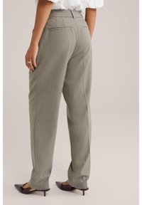 Hallid kohandatud püksid, millel on sile tekstuur, sirge säärega ja kaks tagataskut. Sobitatud terava ninaga tumedate kontsakingadega.