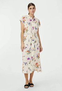 Vestido midi floral em tecido crema suave com mangas curtas, cintura ajustável com laço e padrões coloridos de flores em roxo, laranja e verde. Sandálias de slide pretas.
