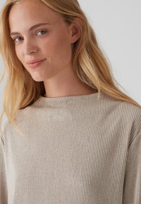 Beige gerippter Pullover mit hohem Kragen und strukturierter Oberfläche. Verfügt über einen weichen Stoff und eine lockere Passform, die durch subtile Stickdetails hervorgehoben wird.