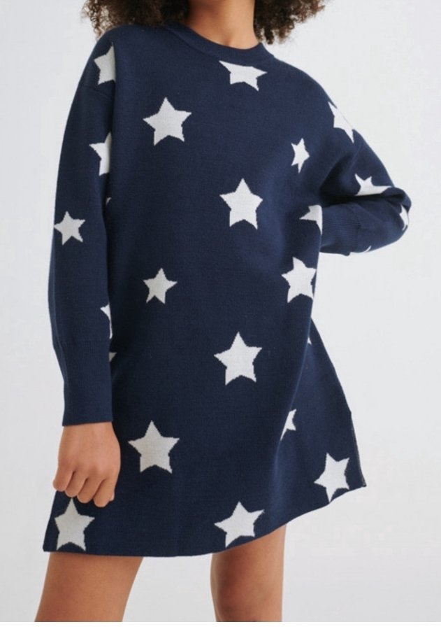 Robe à manches longues bleu marine avec un motif d'étoiles blanches, portée par une personne ayant un bras plié et l'autre détendu le long de son corps.