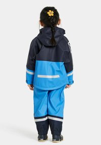 Blå och marinblå vattent ät jacka och byxor designade för barn, med reflexband och huva. Slät yta med ledig passform.