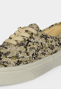 Χαμηλά sneakers Vans με μπεζ και μαύρο λουλουδάτο σχέδιο, κρεμ κορδόνια και λευκή καουτσούκ σόλα.