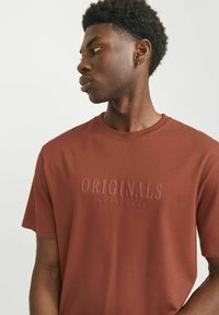 Rudas trumpas rankovės marškinėliai su apvalia apykakle, ant krūtinės esantis tekstūruotas "ORIGINALS JACK & JONES" logotipas šviesesnėje spalvoje.