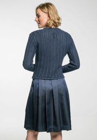Marineblaues Strickjacke mit gerippter Textur und gewelltem Saum, kombiniert mit einem plissierten, gemusterten marineblauen Rock mit glänzender Oberfläche.