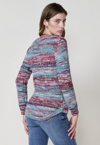 Suéter de punto multicolor con un patrón de rayas en tonos de rosa, azul y púrpura. La textura parece suave y esponjosa, con mangas largas y un dobladillo curvado.