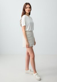 Haut blanc à manches courtes associé à une jupe mini beige et des baskets blanches. La tenue présente des lignes simples et épurées ainsi que des couleurs claires.