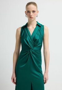 Turkusowa sukienka bez rękawów z gładkiego materiału, z przodem o skręconym wzorze, kołnierzykiem i bocznym rozcięciem dla dodatkowego efektu.