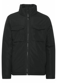 Chaqueta acolchada negra con cuello alto, cremallera frontal y dos bolsillos en el pecho. Textura suave y diseño aislante para mayor calidez.