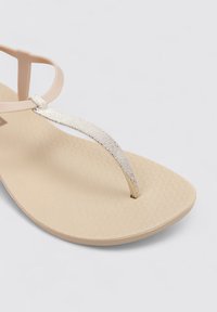 Chancla nude con suela de goma texturizada y una tira de acento dorado metálico. Presenta un diseño tipo thong con un acabado suave.