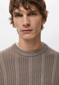 Bruine geribbelde gebreide trui met een ronde hals. Heeft verticale strepen en een gestructureerd patroon. Zacht, middelzwaar materiaal.