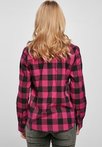 Chemise à carreaux rose et noire à manches longues, vue arrière montrant un ourlet courbé et des détails de poignet à bouton unique.